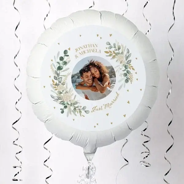 A personalised round wedding balloon featuring a couple’s photo surrounded by floral illustrations, floating against a white backdrop with silver curling ribbons.